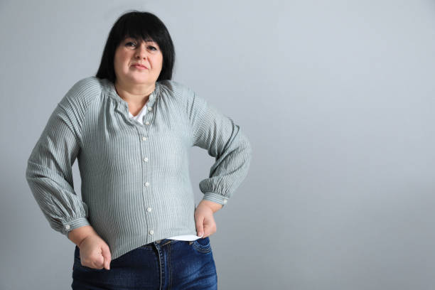 istock Overweight woman in tight shirt on light grey background. Space for text 1437990764