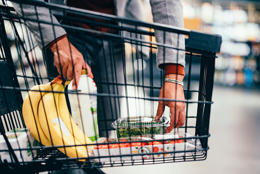 Close up of an unrecognizable man putting groceries into a shopping cart in the supermarket.