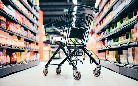 Background and wallpaper of shopping cart in supermarket department store for choosing and buying grocery things at shelf. Time for shopping household goods, snacks, food, fruit, beverages and other.