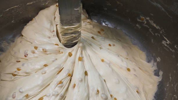 chiudi per la prosess di mescolare la pasta con l'uvetta in una ciotola di metallo, concetto di cibo nutriente. filmati d'archivio. processo di miscelazione dell'impasto crudo in fabbrica. - musica industrial foto e immagini stock