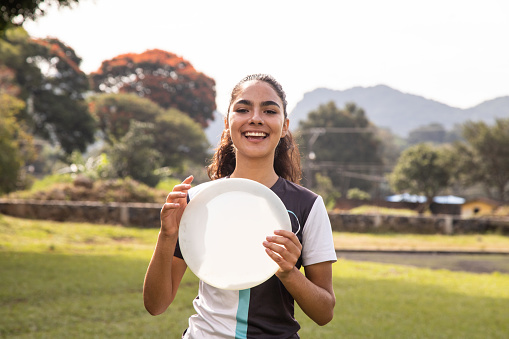 Young girl outdoors with frisbee, smiling and looking at camera