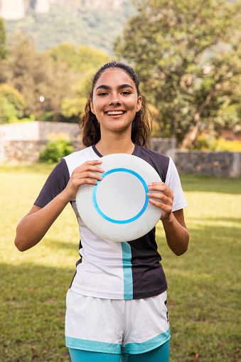 Young girl outdoors with frisbee, smiling and looking at camera