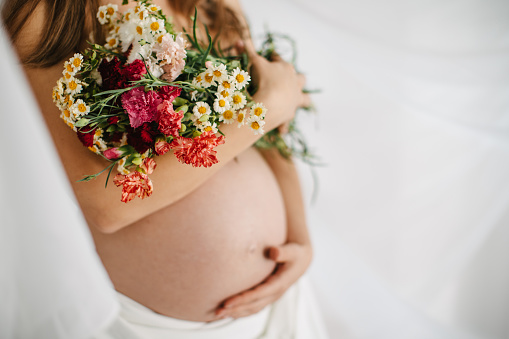 One woman, unrecognizable pregnant woman holding flowers bouquet.