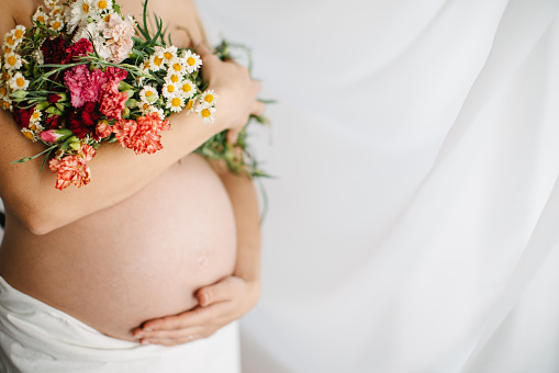 One woman, unrecognizable pregnant woman holding flowers bouquet.
