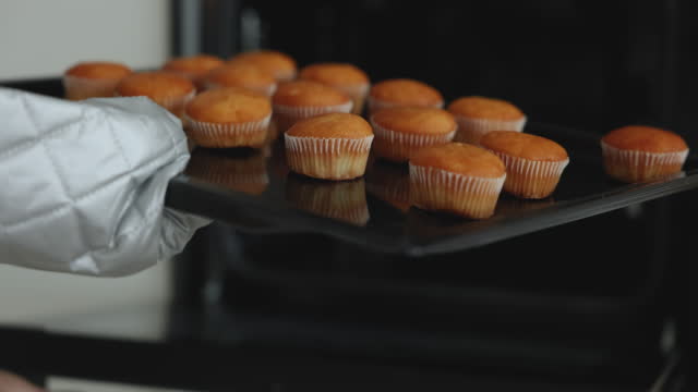 Unrecognizable baker woman taking out tray with cupcakes from oven
