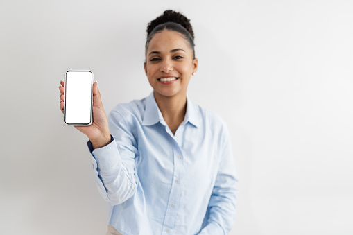 Cheerful African American woman with hair bun smiling and showing smart phone with chroma key screen to the camera. Copy space.