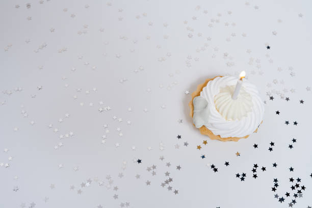istock Festive cupcake with one burning candle on a white plain background with confetti stars. Celebration birthday party. congratulations card 1437999592