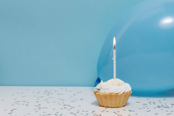 istock Birthday Cupcake with one candle, balloon and festive decor on a blue plain background. Background for your design 1437999842
