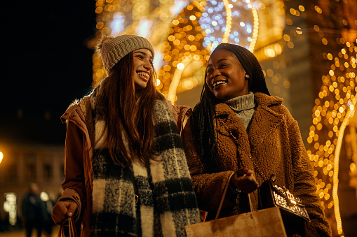 Young beautiful multiracial female friends holding shopping bags and enjoying Christmas shopping in the city