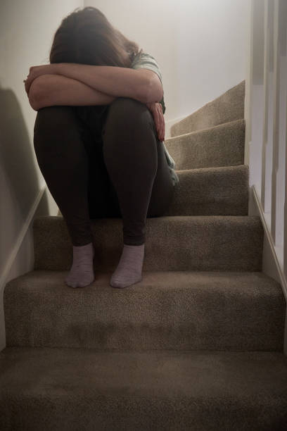 A woman suffering from depression or domestic abuse sat on the stairs of her home hiding her face.