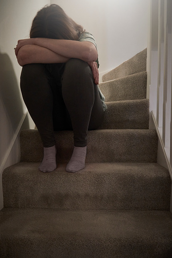 A woman suffering from depression or domestic abuse sat on the stairs of her home hiding her face.