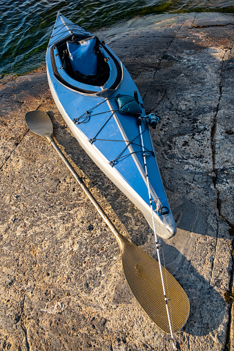 Blue kayak on the stone of a large lake. An oar lies on a rocky shore. Spinning for catching fish on the bow of the boat.