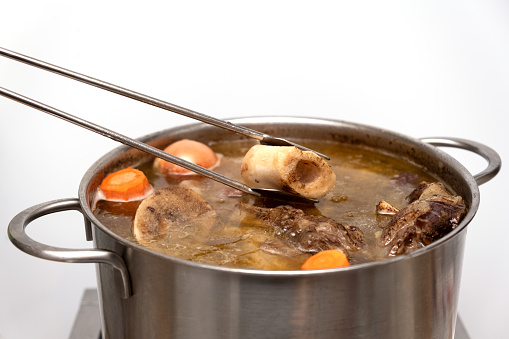 Beef Bone Broth in metal pan, close-up, selective focus. Bones contain collagen, which provides the body with amino acids.