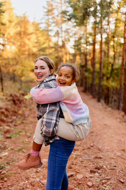 Portrait of a mother an daughter Mother Giving Daughter Piggyback Ride On Walk in the Forest adaptation to nature stock pictures, royalty-free photos & images