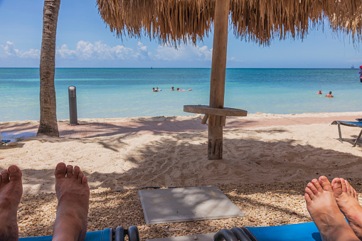 View of feet of man and woman on sunbeds on sandy beach.  Gorgeous turquoise water surface of Atlantic Ocean on background. Aruba.