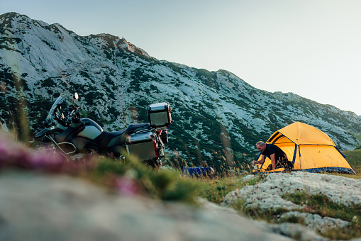A mountain biker sitting around his tent and enjoying on sunset in the mountain peak, preparing food after ride