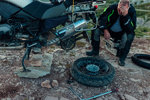 Mature male biker repairing a motorcycle outdoors in mountain
