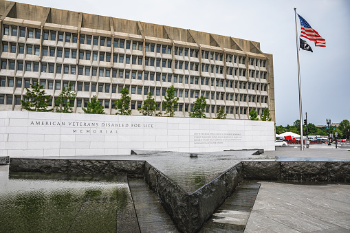Washington, DC USA - June 5, 2019: Entrance sign, reflecting pool and star shaped fountain of the American Veterans Disabled for Life Memorial in front at Health & Human Services building in Washington, DC with American and POW MIA flags