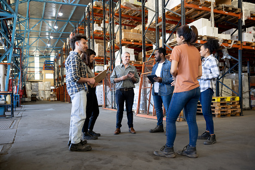 Happy business manager talking to a group of Latin American workers at a distribution warehouse - teamwork concepts