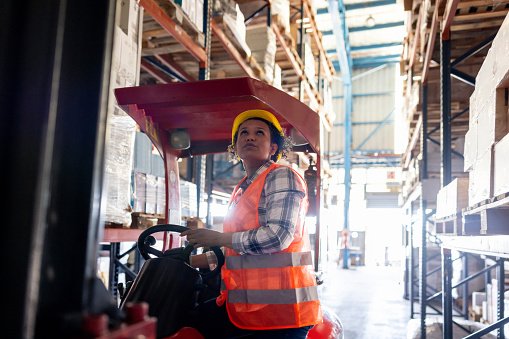 Latin American female worker moving boxes with a forklift at a distribution warehouse