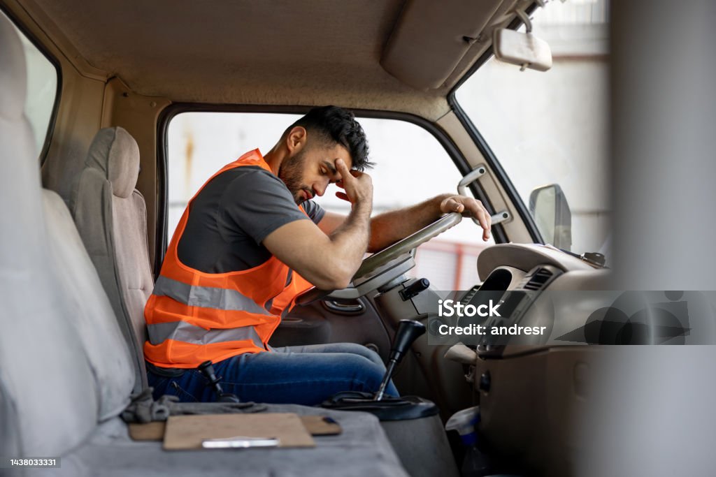 Tired truck driver having a headache after working extra hours Tired truck driver having a headache after working extra hours - transportation crisis Tired Stock Photo