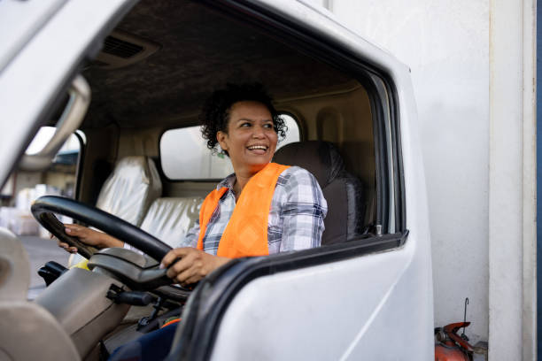 Happy female truck driver smiling while driving Happy Latin American female truck driver smiling while driving her vehicle - freight transportation concepts huge black woman pictures stock pictures, royalty-free photos & images