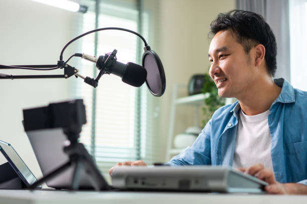 istock Asian attractive audio DJ man speaks into microphone to broadcasting. Young handsome male blogger influencer wearing headphones and recording morning news podcast show for radio at home studio. 1438034087