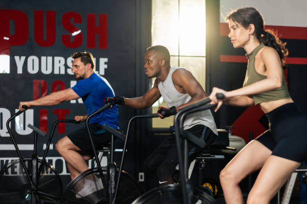 gruppo di giovani atleti che fanno esercizio insieme nella palestra fitness. attraenti sportivi attivi e sportivi si allenano insieme pedalando su una macchina da bici per l'assistenza sanitaria e il benessere nello stadio. - spinning health club instructor gym foto e immagini stock