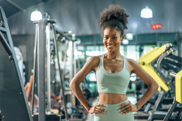 Portrait of African sport girl in sportwear exercising in fitness club. Attractive athlete young female stand and crossing arms after finish workout with machines and equipment in gym or fitness club. stock photo