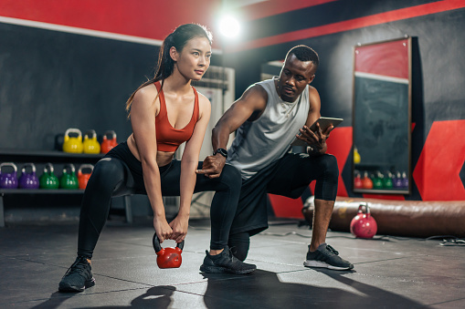 African American trainer motivate young sportsgirl to exercise in gym. Instructor coach teach Caucasian girl lift weight dumbbell for biceps to improve strength and maintain muscle at fitness club.