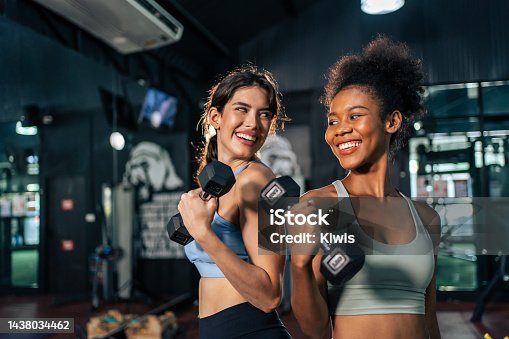 istock Latino and African sport woman exercising and build muscle in stadium. Active strong beautiful fit athlete girls in sportswear workout lifting weight dumbbell for arm and health care at fitness club. 1438034462
