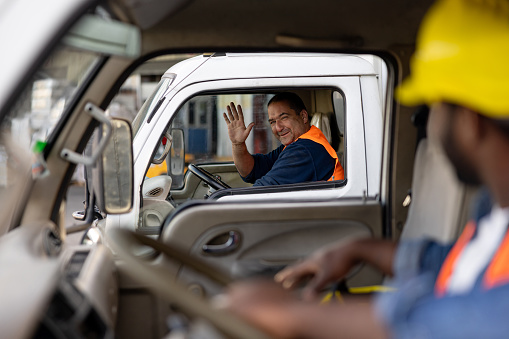 Happy Latin American truck driver greeting another one while driving and waving his hand - freight transportation concepts