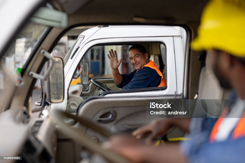 Happy truck driver greeting another one while driving Happy Latin American truck driver greeting another one while driving and waving his hand - freight transportation concepts Truck Driver Stock Photo