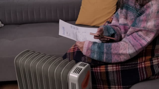 Woman near heater with smartphone and bills, energy crisis concept