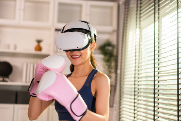 istock Asian sportswoman using innovative technology VR glasses for exercise. Attractive beautiful girl wearing virtual reality headset and holding gaming controller while doing boxing fight workout at home. 1438035522