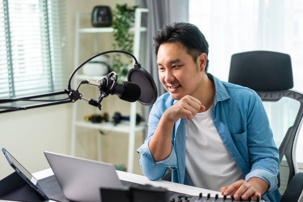 istock Asian attractive audio DJ man speaks into microphone to broadcasting. Young handsome male blogger influencer wearing headphones and recording morning news podcast show for radio at home studio. 1438035539