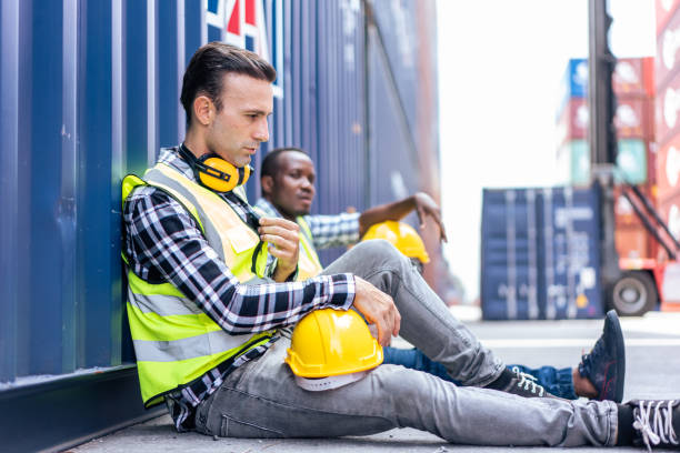 Caucasian man worker taking a break after working in container port. Attractive foreman engineer sitting on floor and resting while processes order and product at warehouse logistic in cargo freight.