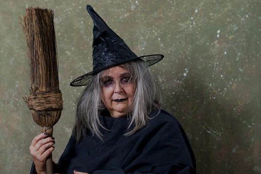 close-up of a white-haired witch with her broom against an abstract background