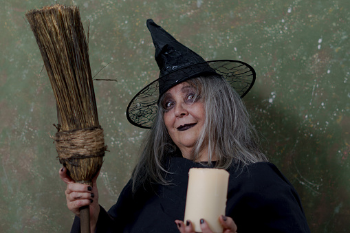 close-up of a white-haired witch with her broom and a white candle on an abstract background halloween celebration