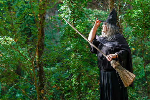 close-up of white-haired witch with hat in profile in the forest with her broom