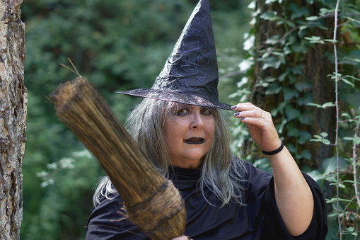 close-up of white-haired witch with hat and broom in forest background