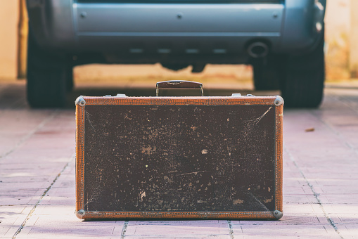 Old shabby leather suitcase by the car
