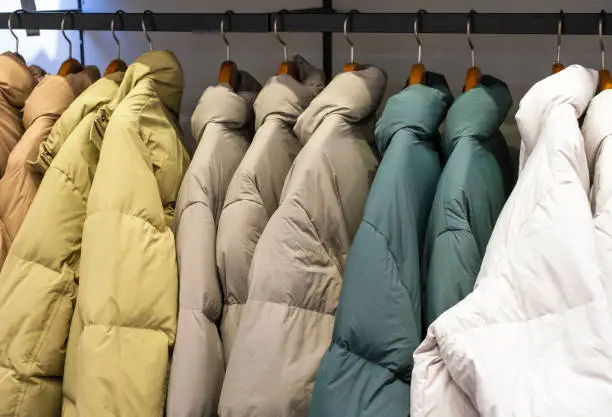 Photo of Multicolored winter down jackets hanging on hangers in the store close-up, side view.