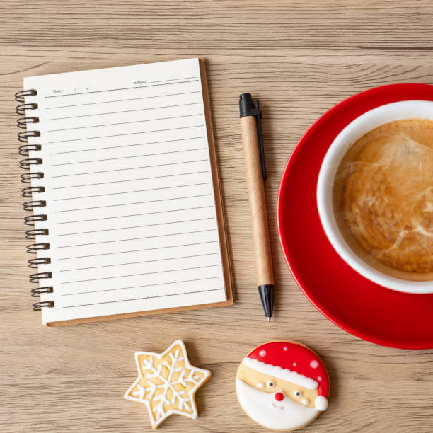 Opened notebook with pen, transparent cup of coffee and chocolate chip cookies on a light wooden table background, top view