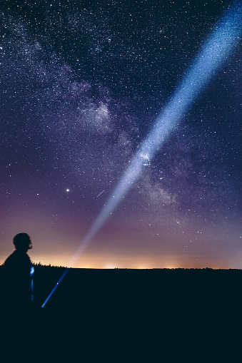A vertical shot of a person pointing the flashlight at the sky with the Milky Way Galaxy
