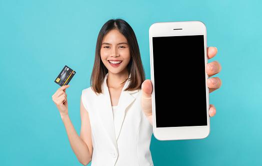 Studio shot of Beautiful Asian woman holding smartphone mockup of blank screen and show credit card on blue background.