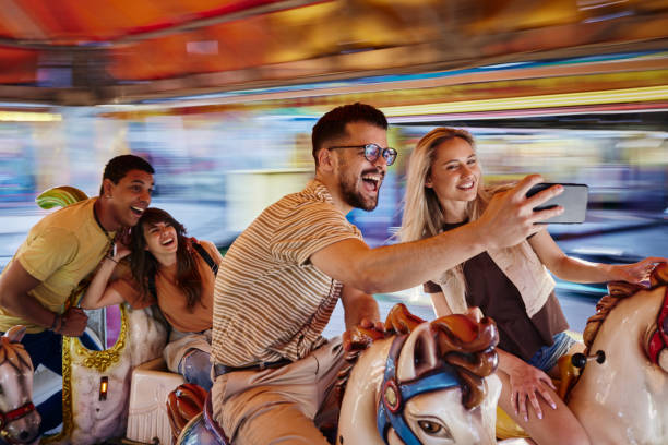 Happy friends taking a selfie during carousel ride at amusement park.