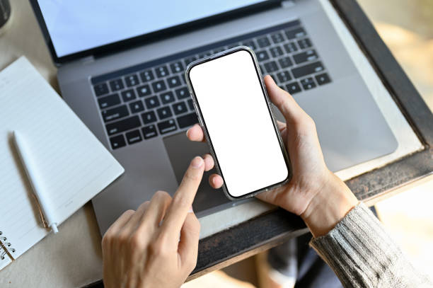 istock A man holding a smartphone mockup over laptop computer on a desk. close-up image 1438065909