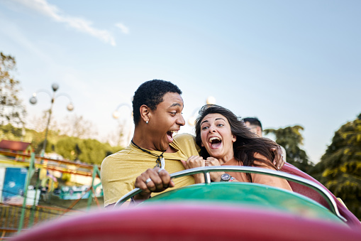 Young cheerful couple having fun on rollercoaster at amusement park. Copy space.