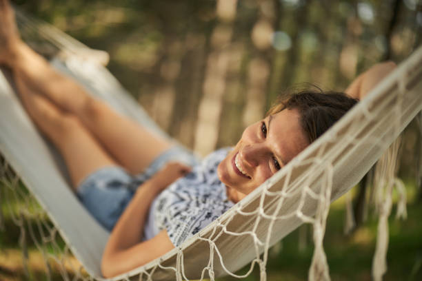 Happy woman relaxing in hammock in the forest. Young happy woman day dreaming while relaxing in hammock in nature. hammock relaxation women front or back yard stock pictures, royalty-free photos & images